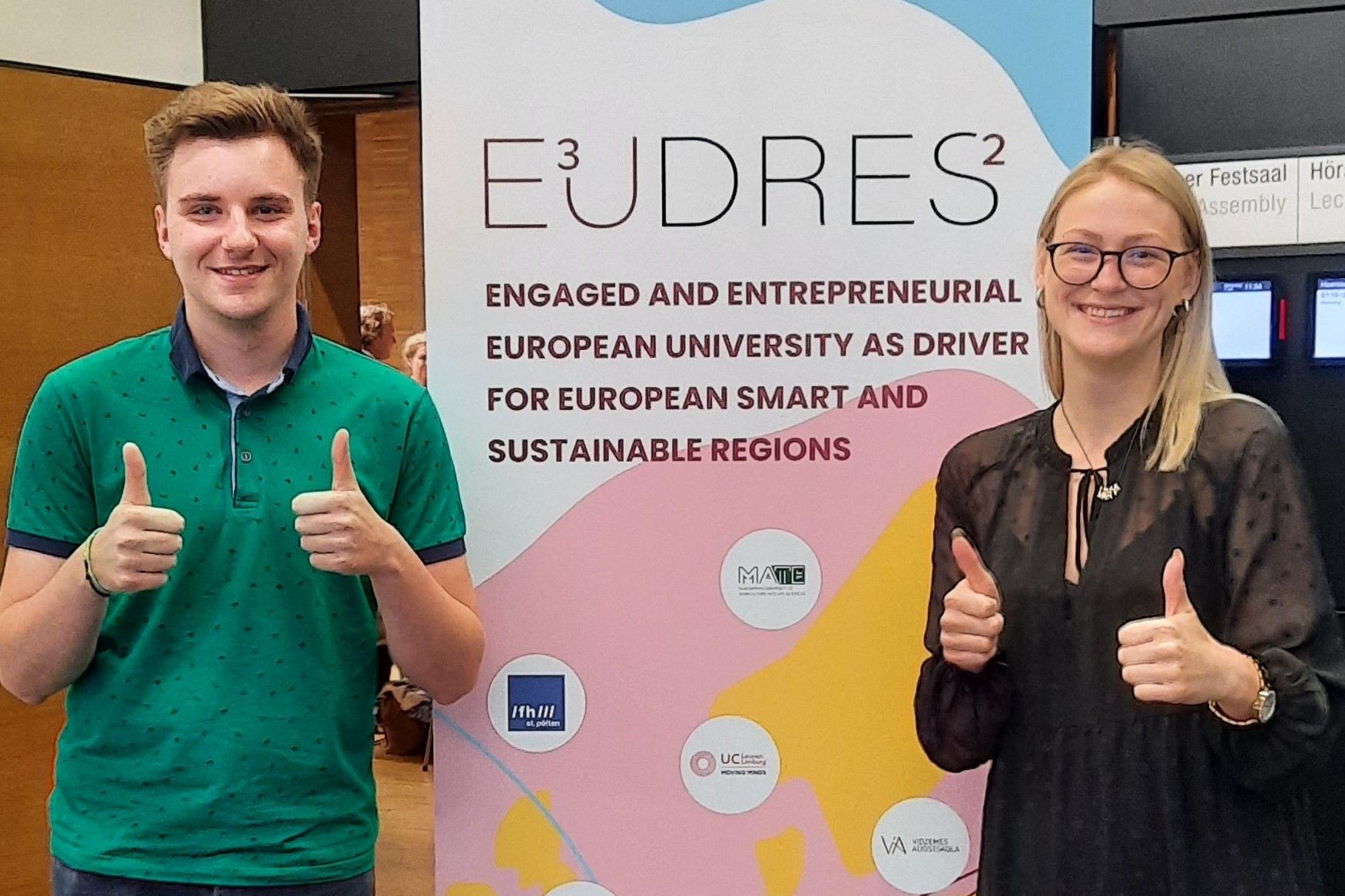 People walking through a bright indoor hallway with glass walls and shops.