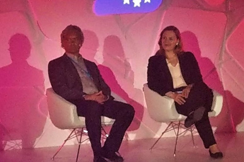 People walking through a bright indoor hallway with glass walls and shops.