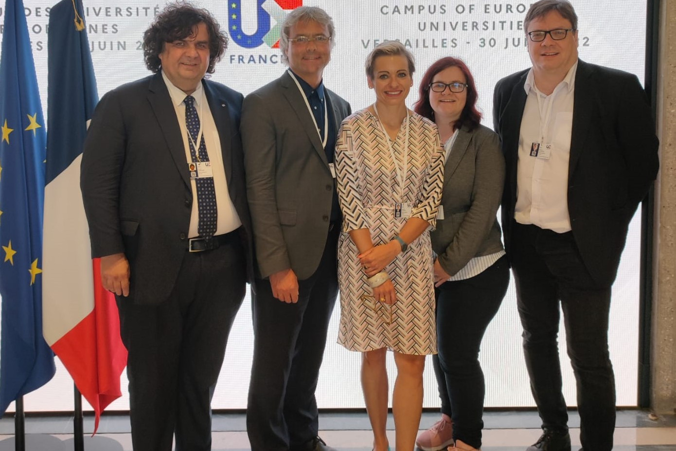 People walking through a bright indoor hallway with glass walls and shops.