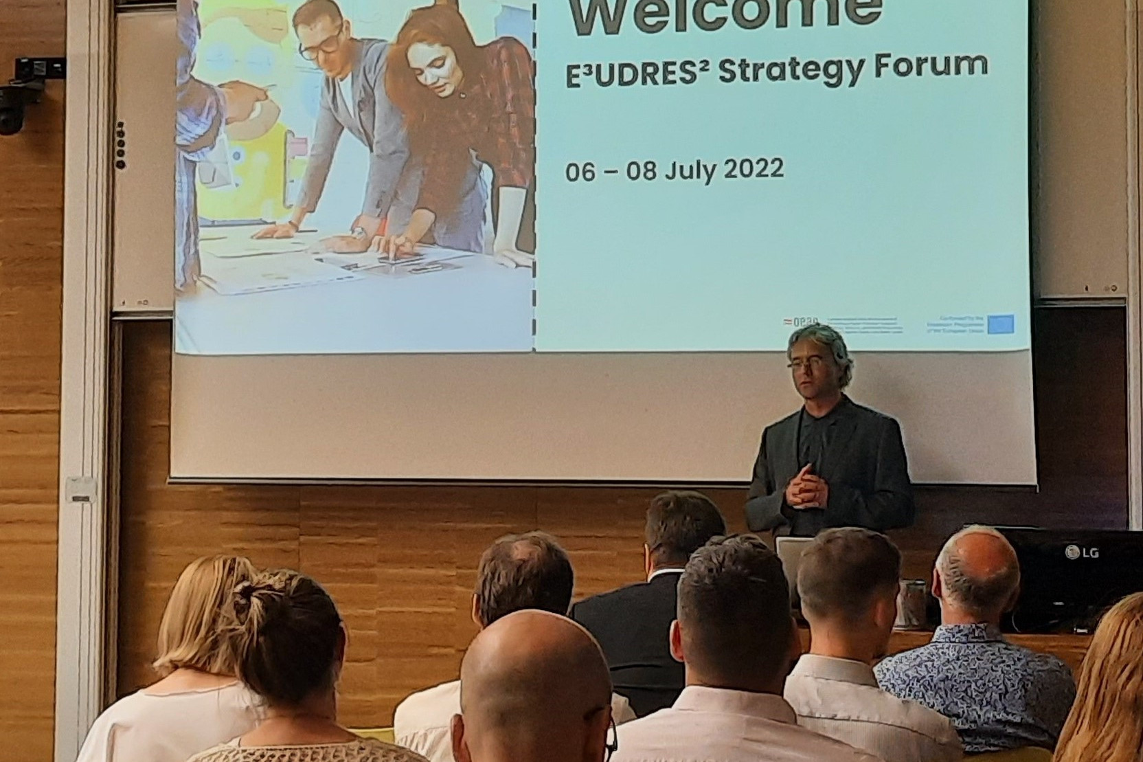 People walking through a bright indoor hallway with glass walls and shops.