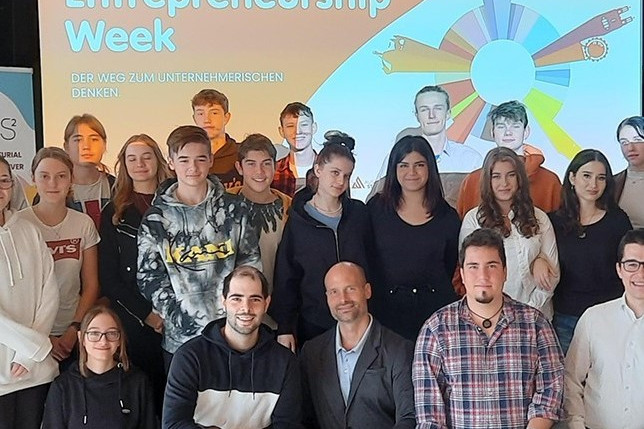 People walking through a bright indoor hallway with glass walls and shops.