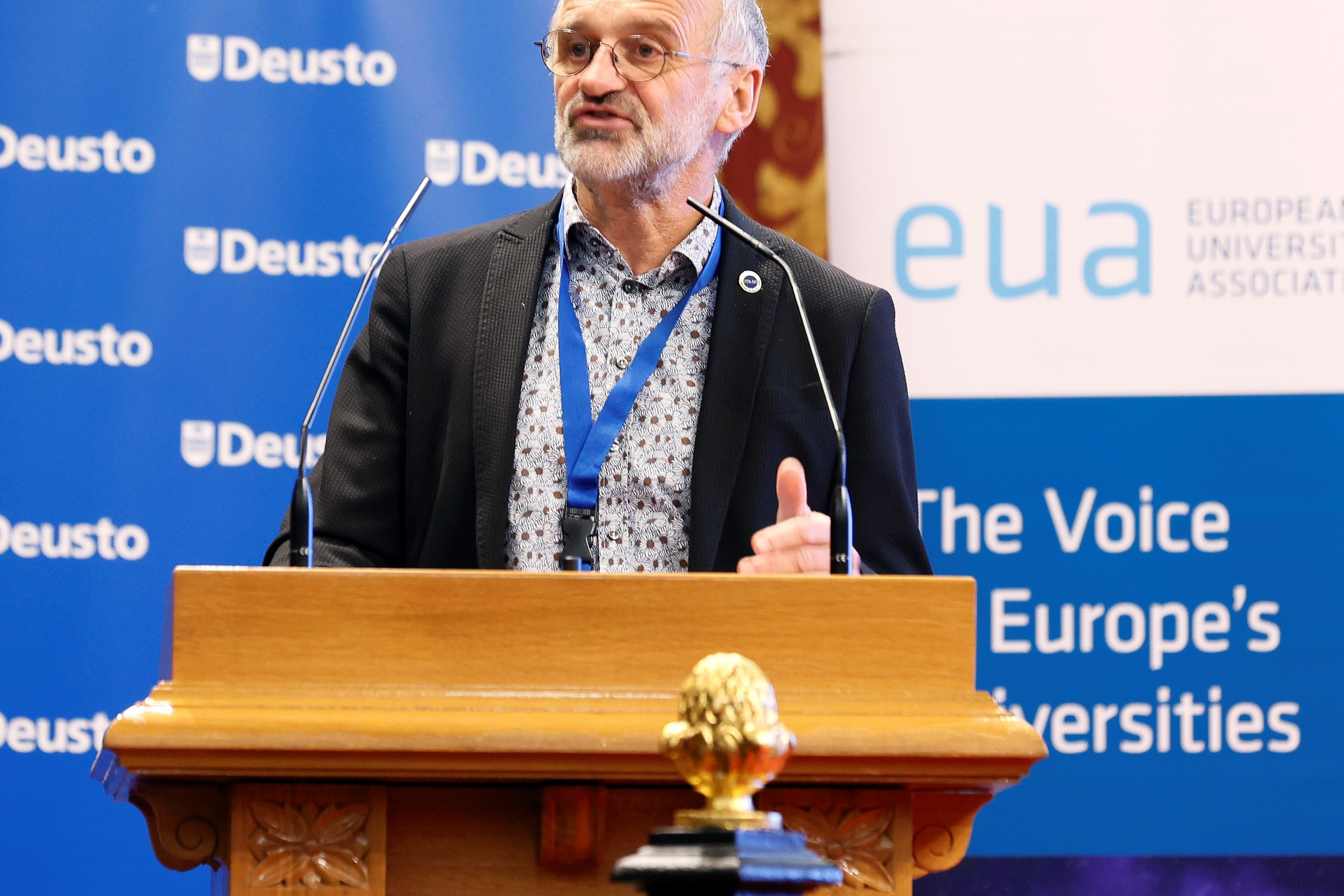 People walking through a bright indoor hallway with glass walls and shops.