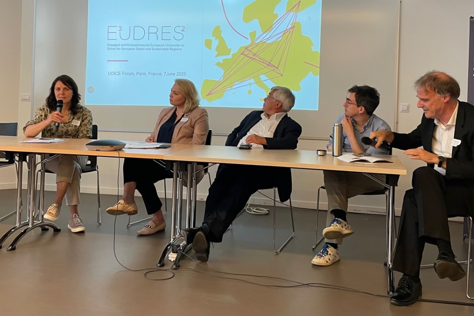 People walking through a bright indoor hallway with glass walls and shops.