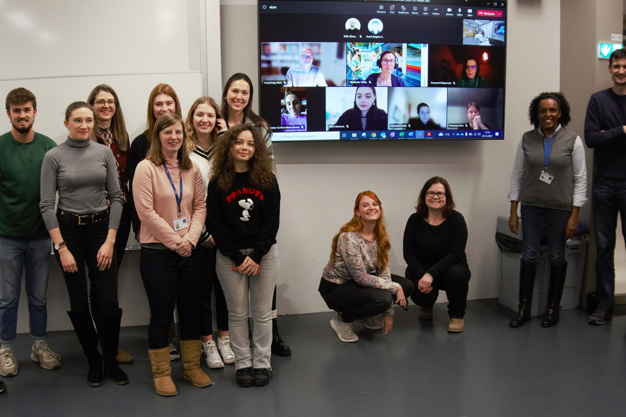 Group of people posing in front of a screen showing participants in a hybrid meeting.