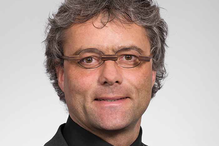 People walking through a bright indoor hallway with glass walls and shops.