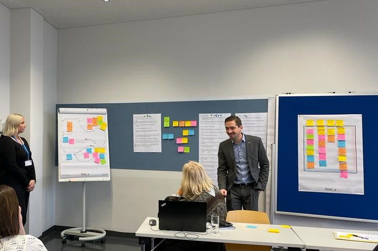 People walking through a bright indoor hallway with glass walls and shops.